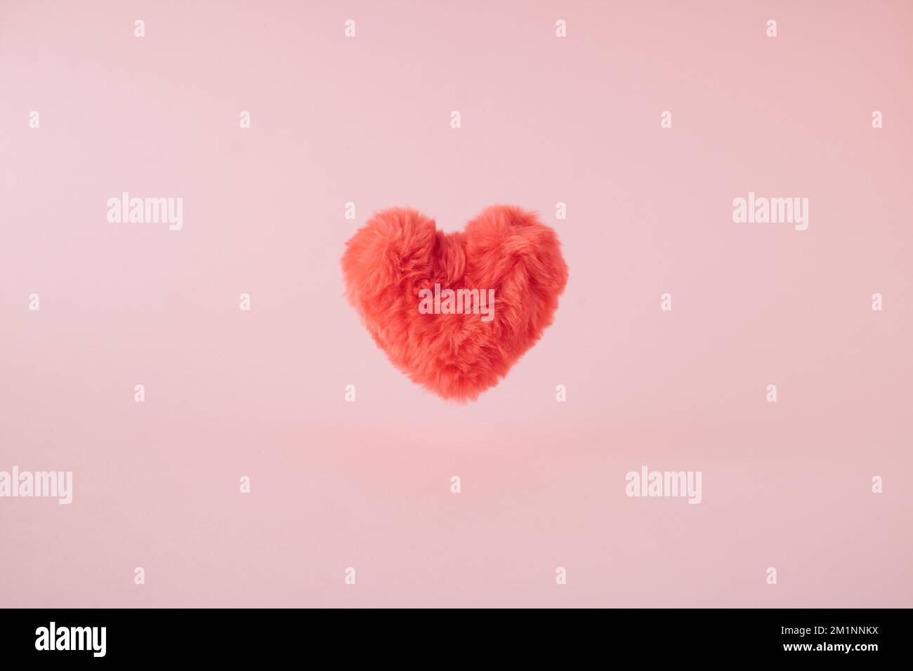 Rosafarbenes, flauschiges Herz schwebt über pastellfarbenem Hintergrund. Stockfoto
