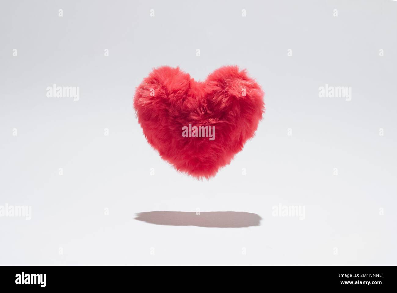 Rosafarbenes, flauschiges Herz schwebt über weißem Hintergrund. Stockfoto