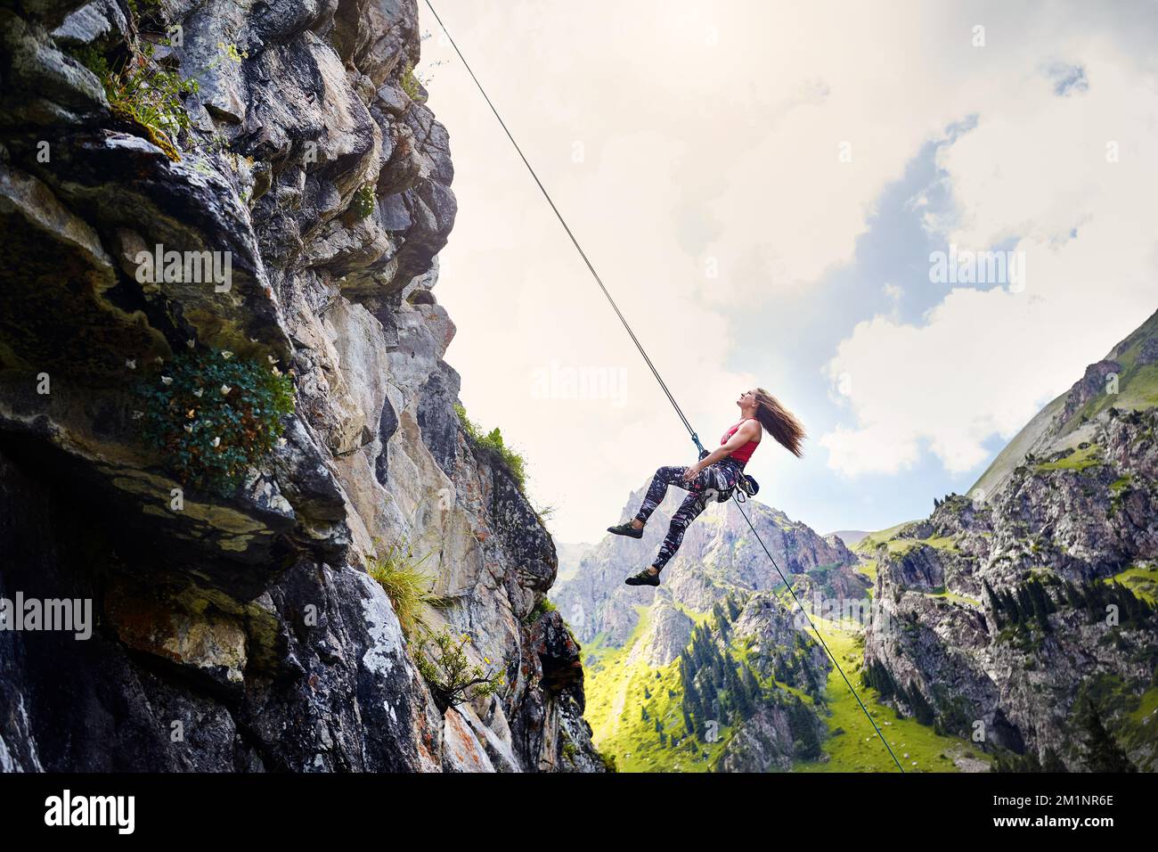 Fit, starke Kletterfrau, die in der Luft in der Nähe von hohen vertikalen Felsen mit Seilen in den Bergen Kasachstans fliegt Stockfoto