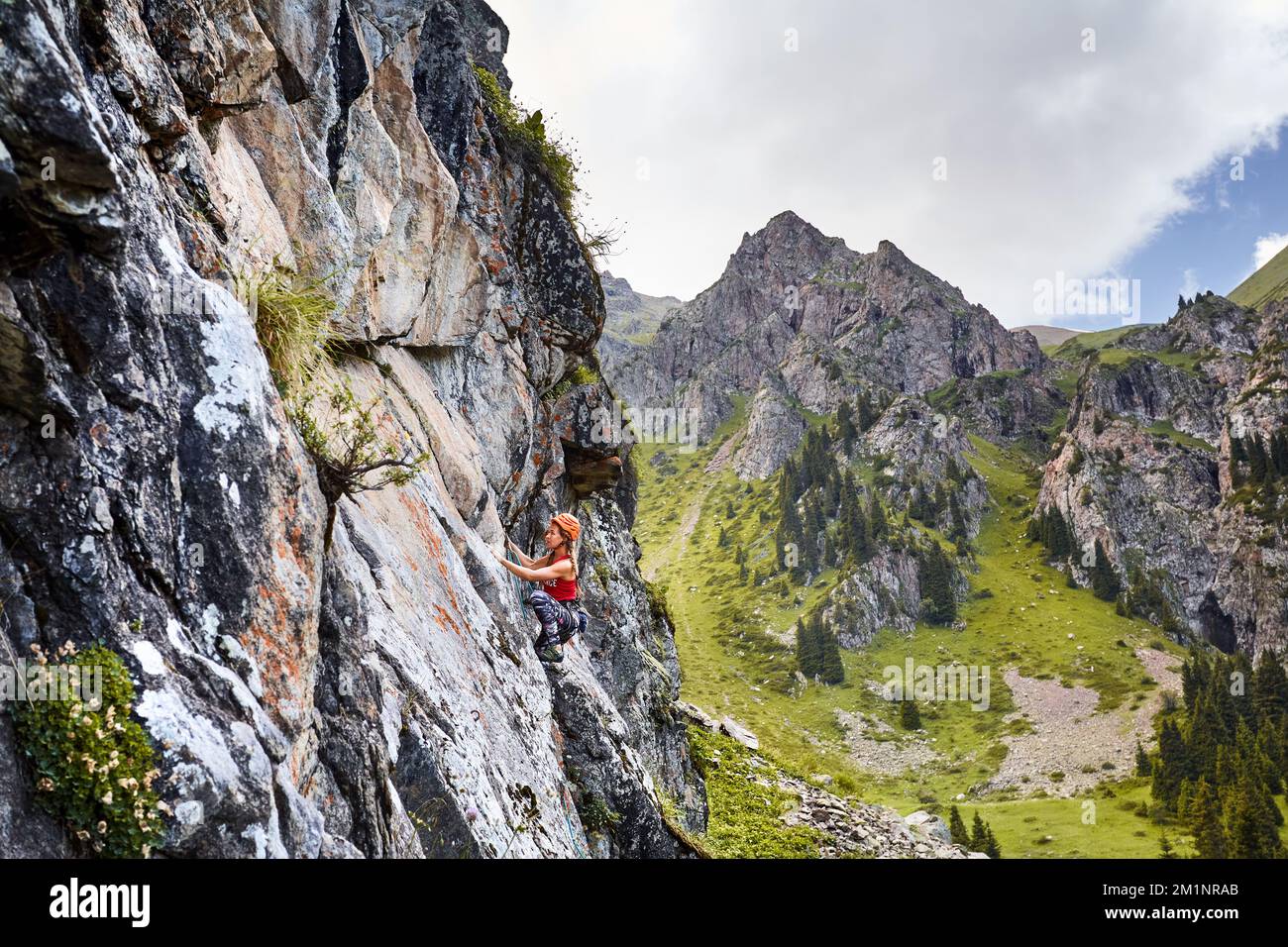 Porträt von Fit Strong Woman in roter Hose und Helm beim Klettern auf den hohen vertikalen Felsen in den Bergen Tyan Shan in Kasachstan Stockfoto