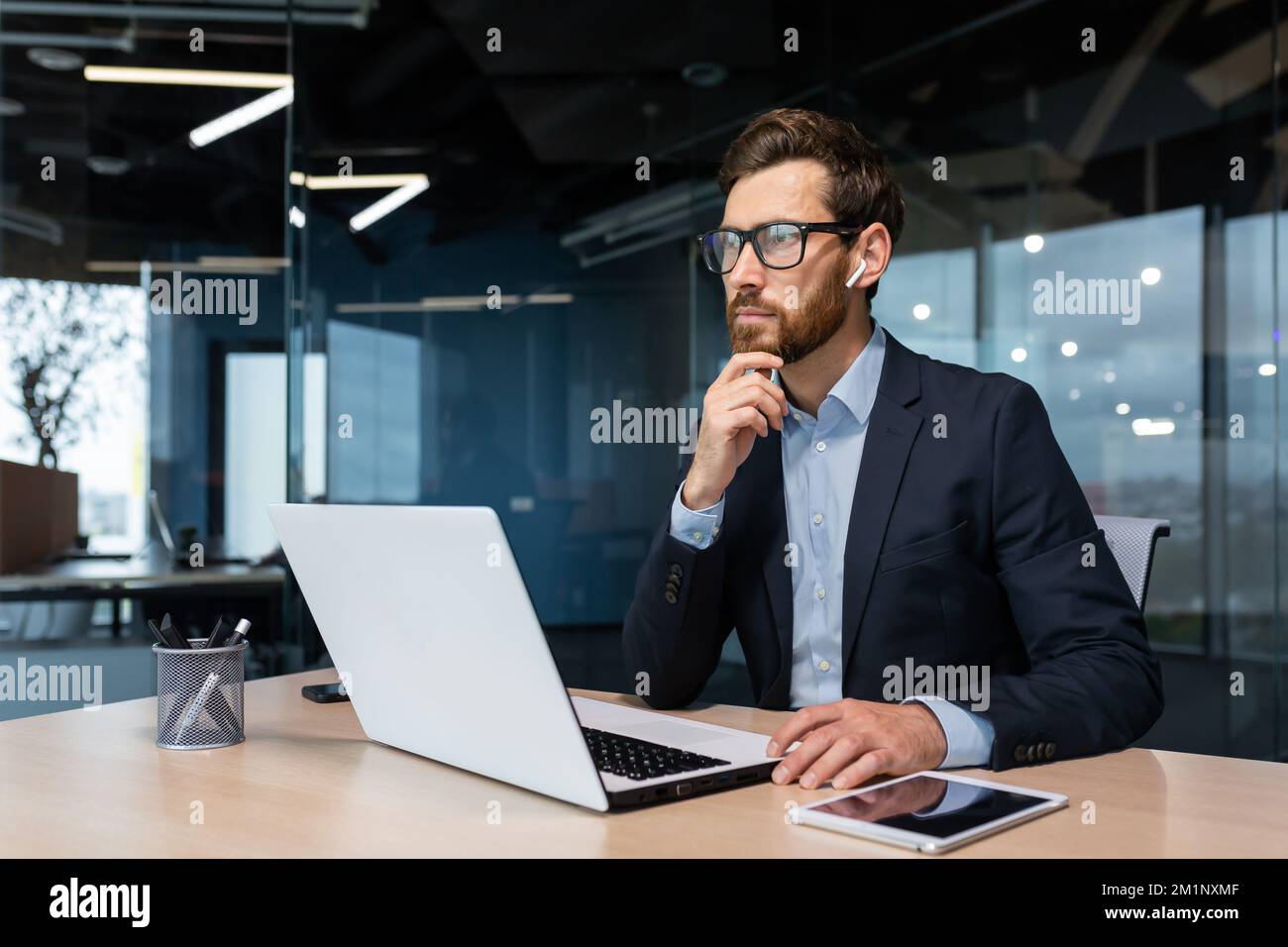 Ein aufmerksamer und seriöser junger Geschäftsmann, Freiberufler, Designer und Architekt arbeitet im Büro an einem Laptop mit Kopfhörern. Stockfoto