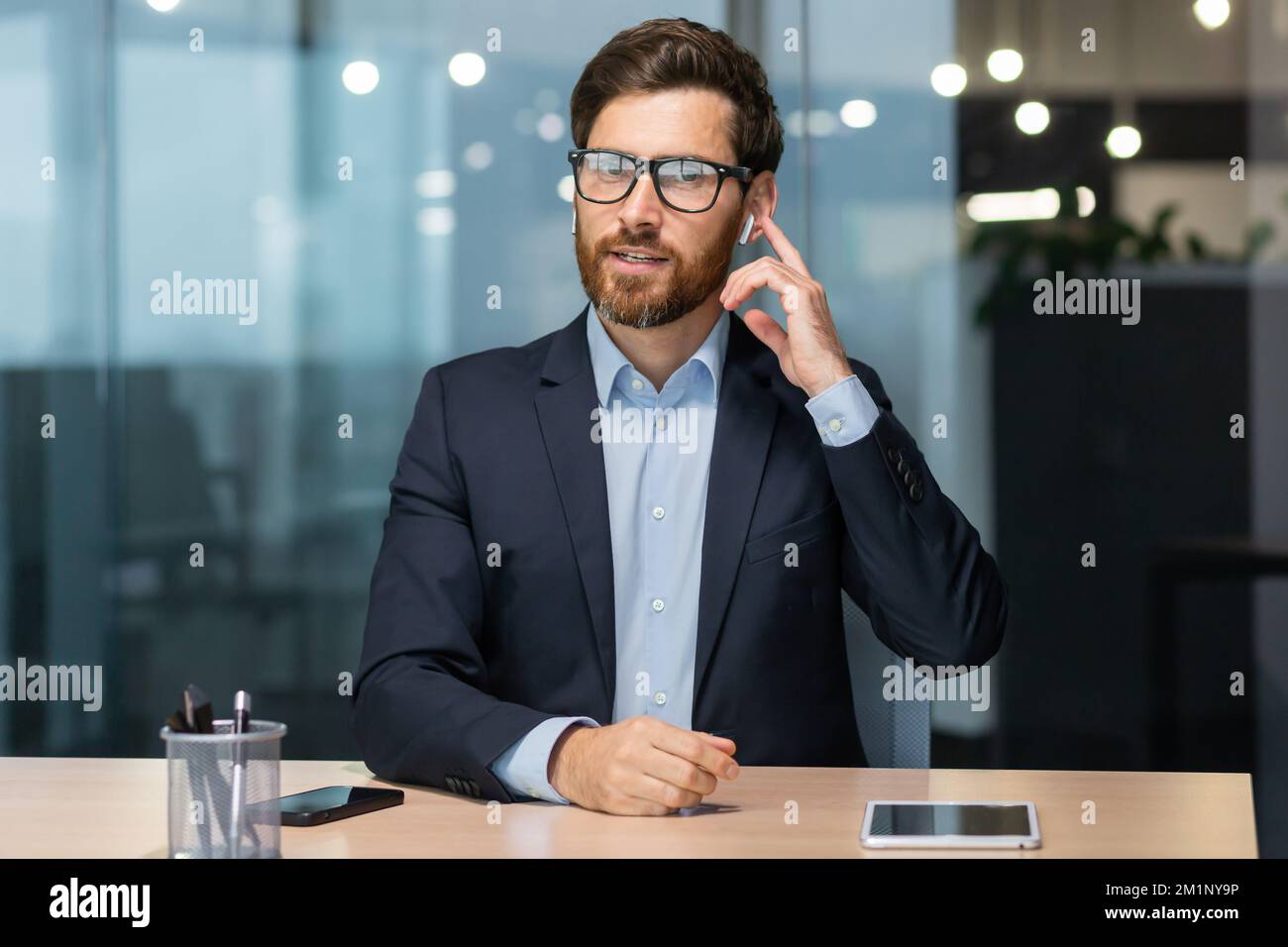 Porträt eines jungen Beraters, Geschäftsmann. Im Büro am Tisch sitzen, mit der Kamera sprechen, Kopfhörer halten, Geschäftskonferenz, Kundendienst. Stockfoto
