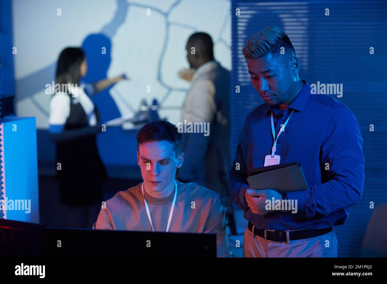 Porträt von zwei Personen, die im Kontrollzentrum arbeiten, mit futuristischen Blau- und Rottönen Stockfoto