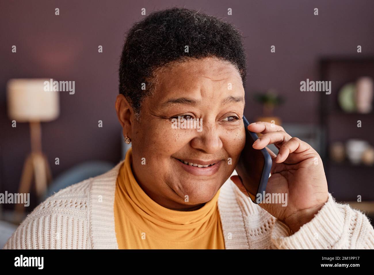 Nahaufnahme des Porträts einer schwarzen Seniorin, die zu Hause per Smartphone anruft und mit ihren Lieben fröhlich lächelt Stockfoto