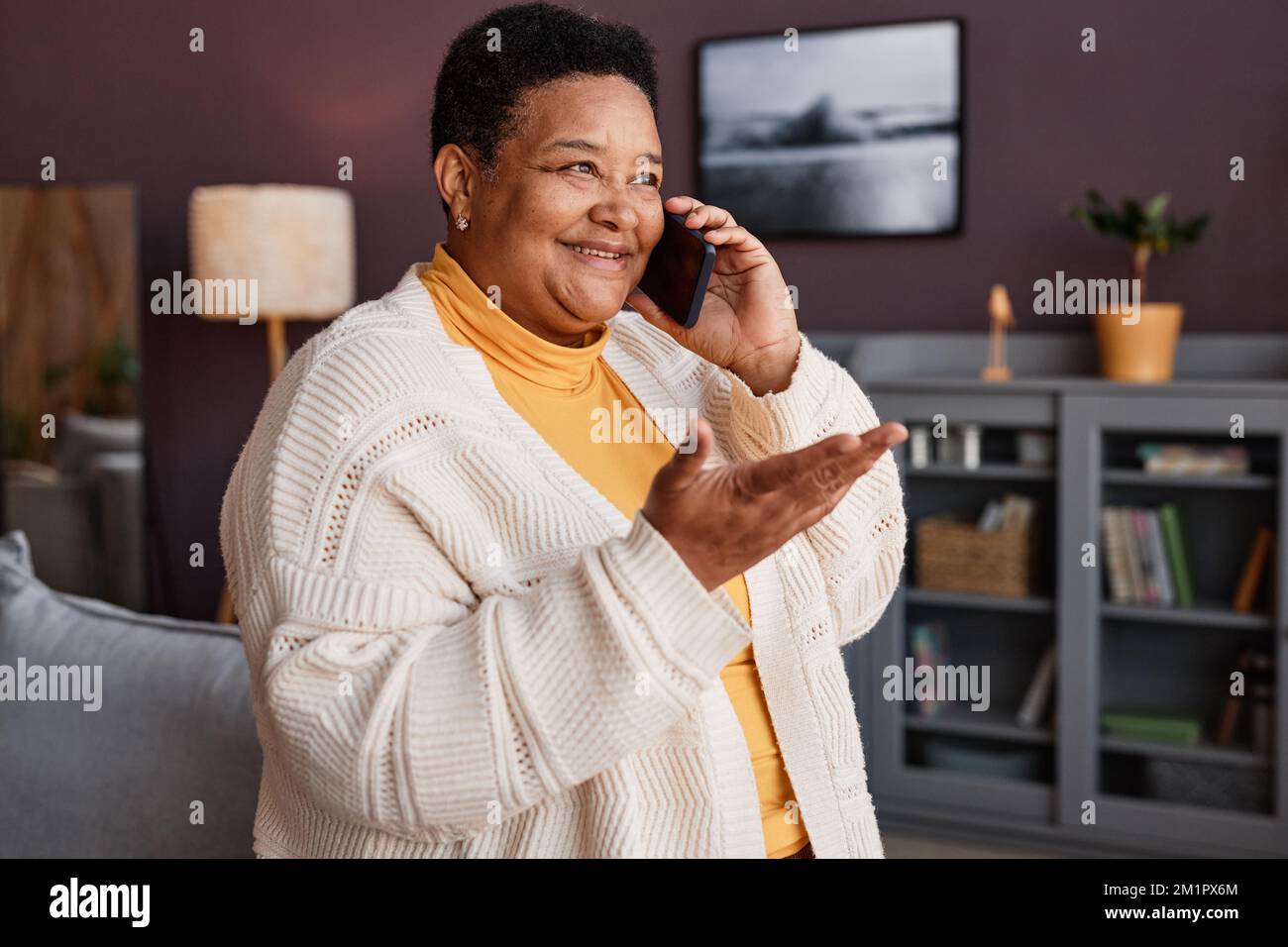 Porträt einer fröhlichen Seniorengroßmutter, die zu Hause telefoniert und Gesten macht Stockfoto