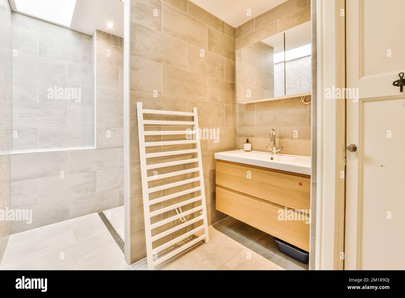 Ein modernes Badezimmer mit beigefliesten Wänden und weißen Fliesen an der Wand, es gibt einen Handtuchhalter neben dem Waschbecken Stockfoto