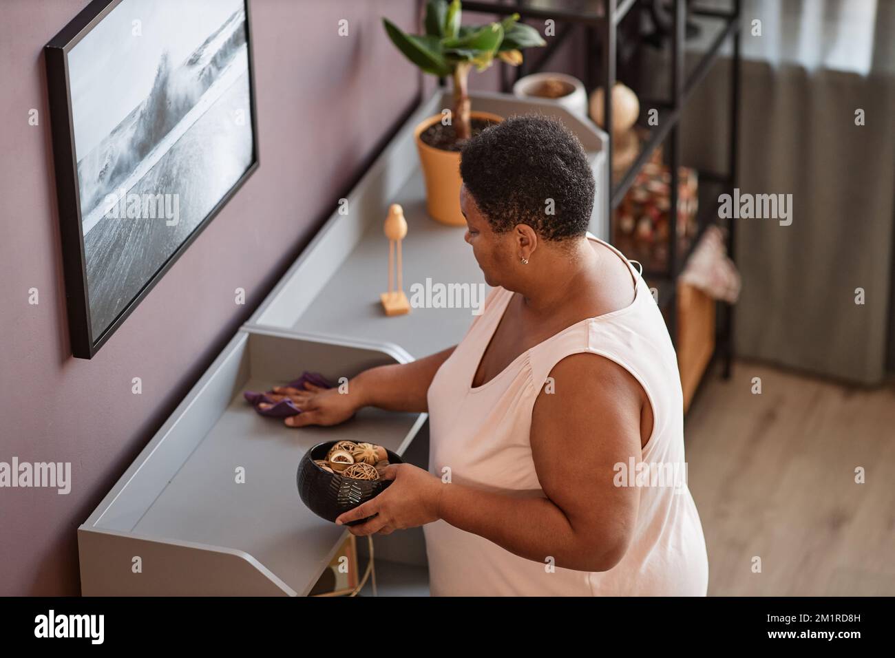 Hochwinkelporträt einer schwarzen Seniorin, die Regale in modernen Wohnräumen staubt, Kopierraum Stockfoto