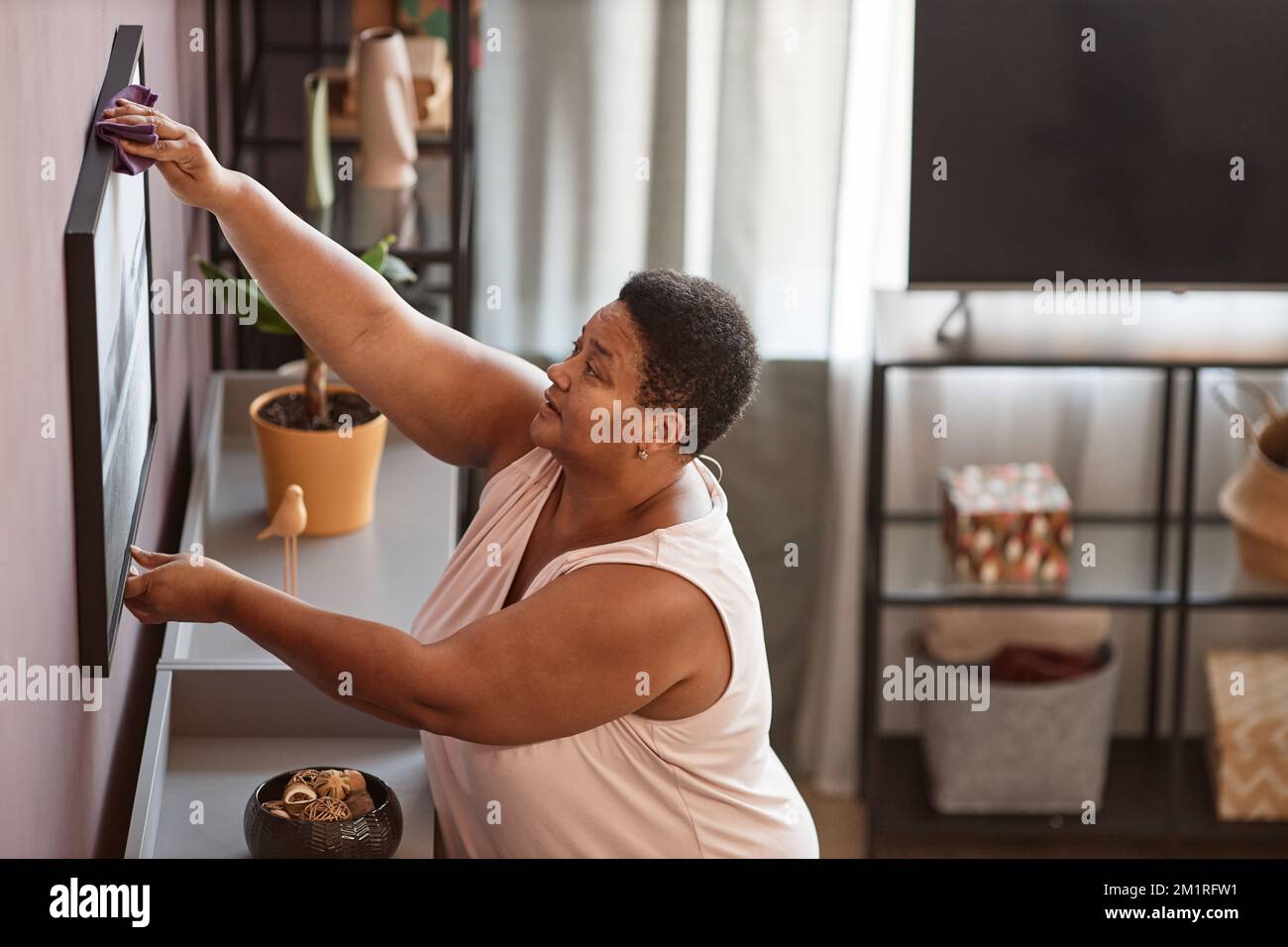 Seitliches Porträt einer Seniorin, die das Haus putzt und die Wände abstaubt, Kopierraum Stockfoto