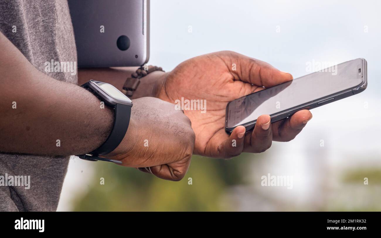 Ein afrikanischer Schwarzer zeigt mit dem Finger auf ein Smartphone in der Stadt, schreibt SMS auf einem Handy, glitzernder Straßenleben, verschwommener Hintergrund Stockfoto