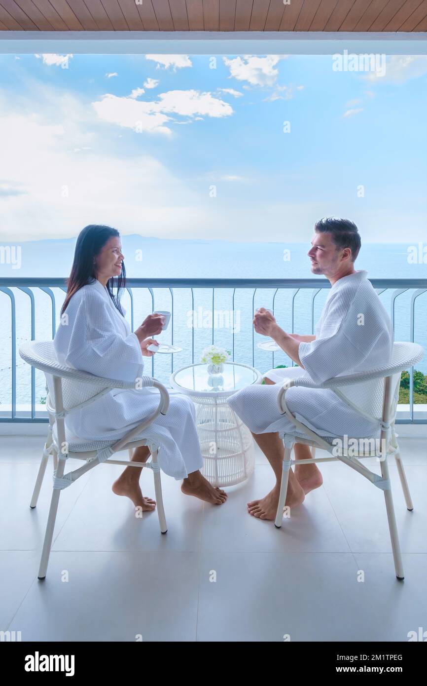 Ein paar asiatische Frauen und weiße Männer trinken Kaffee in einem Hotel auf dem Balkon mit Blick auf das Meer in Thailand Stockfoto