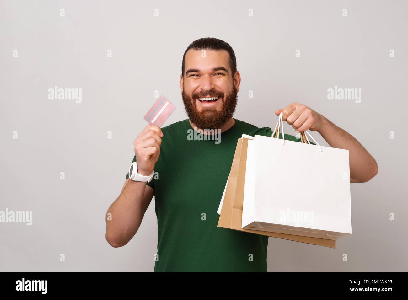 Der junge bärtige Mann ist froh, dass er jetzt mit seiner Karte für seine Einkäufe in Einkaufstaschen bezahlen kann. Stockfoto