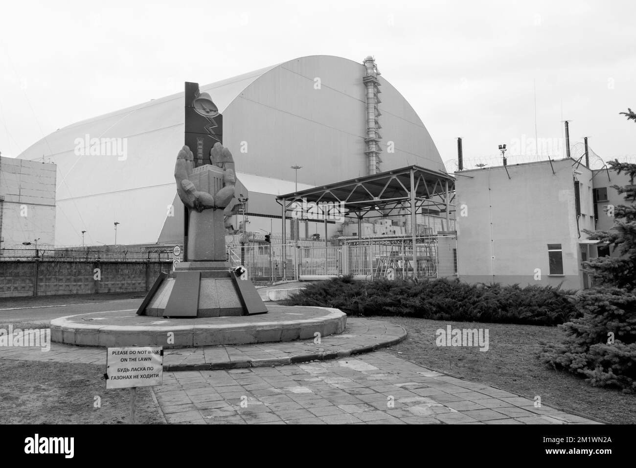 Denkmal der Tschernobyl-Liquidatoren vor einem großen Kuppelcontainer mit 4. Reaktor am Explosionsort des kernkraftwerks tschernobyl. Schwarzweißfotografie Stockfoto