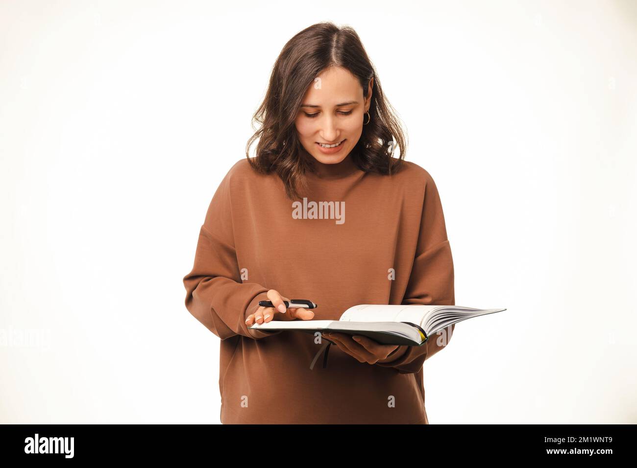 Junge schöne Frau hält ein Tagebuch und schreibt darin mit einem Stift auf weißem Hintergrund. Stockfoto