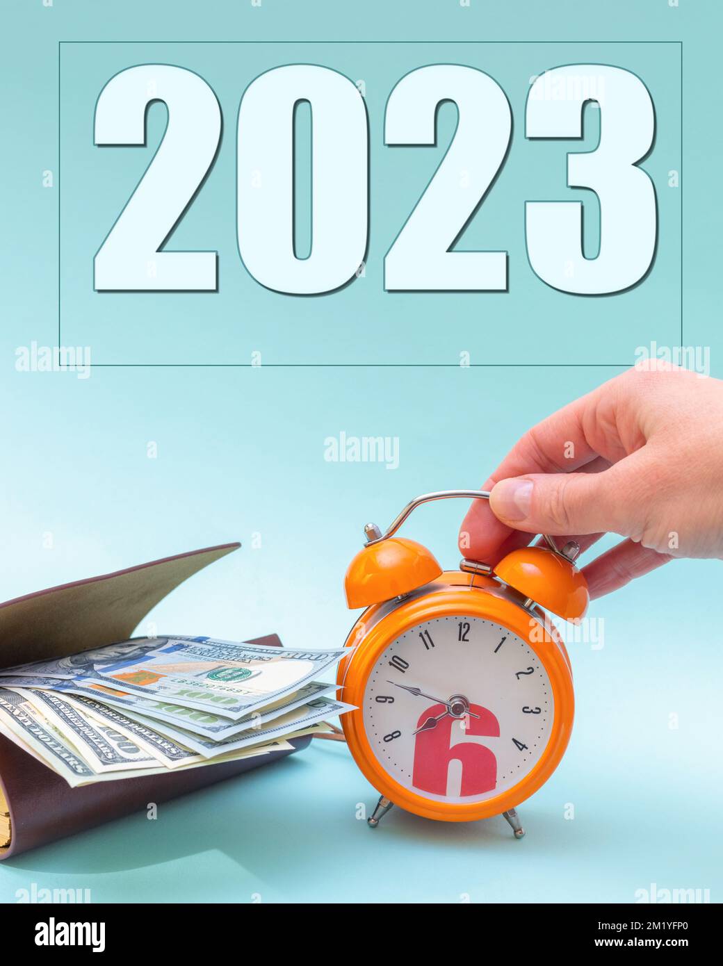 Neujahr 2023. Eine Hand hält einen orangefarbenen Wecker neben einem Geldbeutel mit US-Dollar und dem Jahr 2023. Das Konzept des Wandels. Geschäftskonzept. Der Betrug Stockfoto