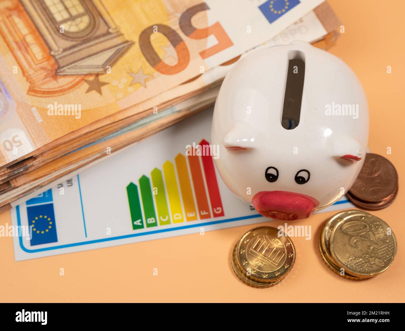 Geld, Sparschwein und Energieeffizienzzertifikat auf orangefarbenem Hintergrund. Geschäftsmann spart Geld mit guter Energieklasse. Euro-Banknoten in Papierform Stockfoto