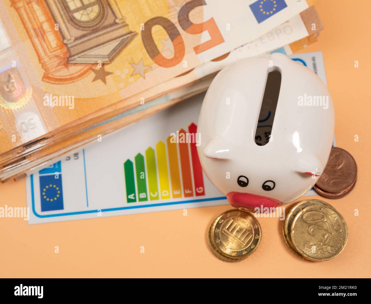 Geld, Sparschwein und Energieeffizienzzertifikat auf orangefarbenem Hintergrund. Geschäftsmann spart Geld mit guter Energieklasse. Euro-Banknoten in Papierform Stockfoto