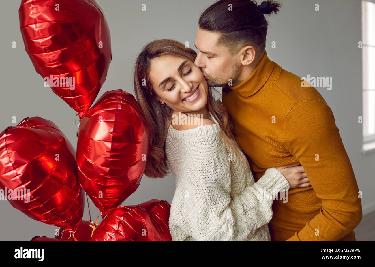 Ein junges glückliches Paar umarmt und küsst sich mit herzförmigen Ballons Stockfoto