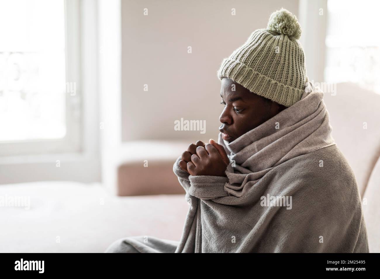 Eiskalter junger schwarzer Mann, der auf der Couch im Wohnzimmer sitzt Stockfoto