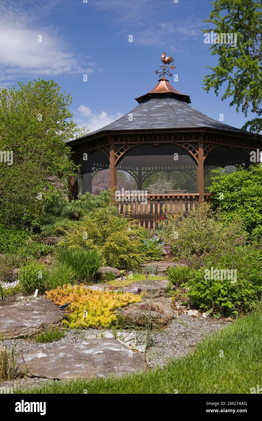 Pavillon und grenzt im Frühling an gemischte Pflanzen und Sträucher im landschaftlich gestalteten Garten. Stockfoto