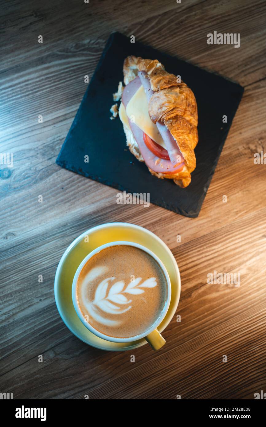 Frischer Cappuccino oder Latte-Kaffee mit Croissant-Sandwich auf Holztisch im Café Stockfoto