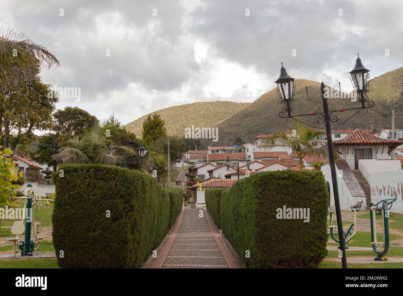 Die Sommerszene in der kolumbianischen Stadt Guatavita mit einer Torfstraße aus Kiefernholz, Gärten und Bergen im Hintergrund. Stockfoto