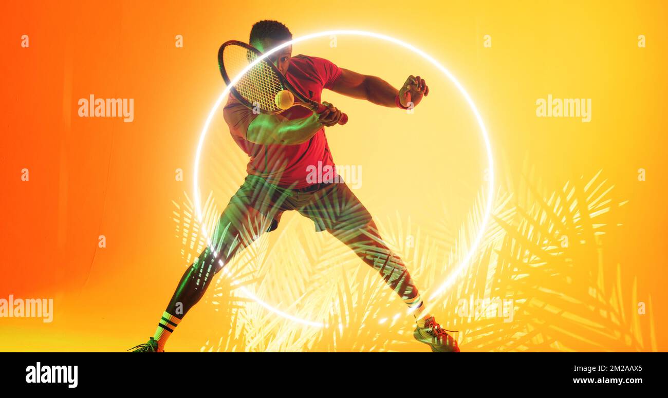 Ein afroamerikanischer Tennisspieler schlägt mit einem Schläger an einem beleuchteten Kreis und Pflanzen Stockfoto