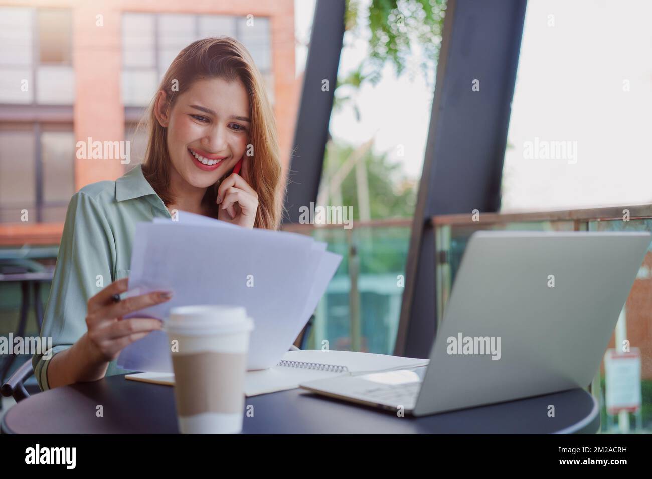 Junge Geschäftsfrau, die mit Zeitungen arbeitet und am Handy telefoniert, Finanzdokumente liest, während sie im Café sitzt. Stockfoto