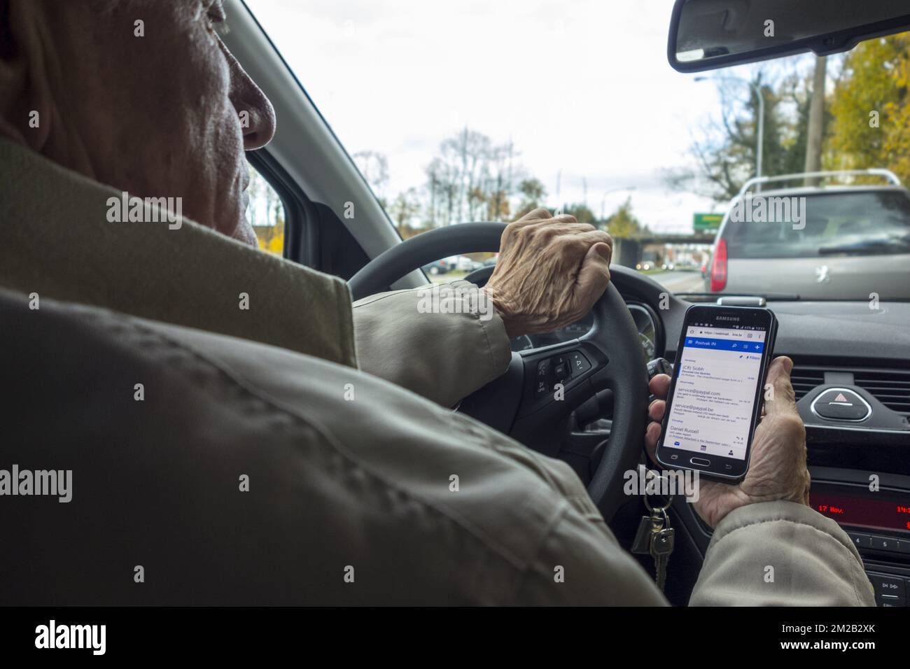 Verantwortungsloser alter Mann am Lenkrad, der Nachrichten auf Smartphone/Smartphone/Mobiltelefon abfragt, während er mit dem Auto unterwegs ist | Homme agé derrière volant lisant Nachrichten sur Smartphone/téléphone mobile en roulant en voiture 17/11/2017 Stockfoto