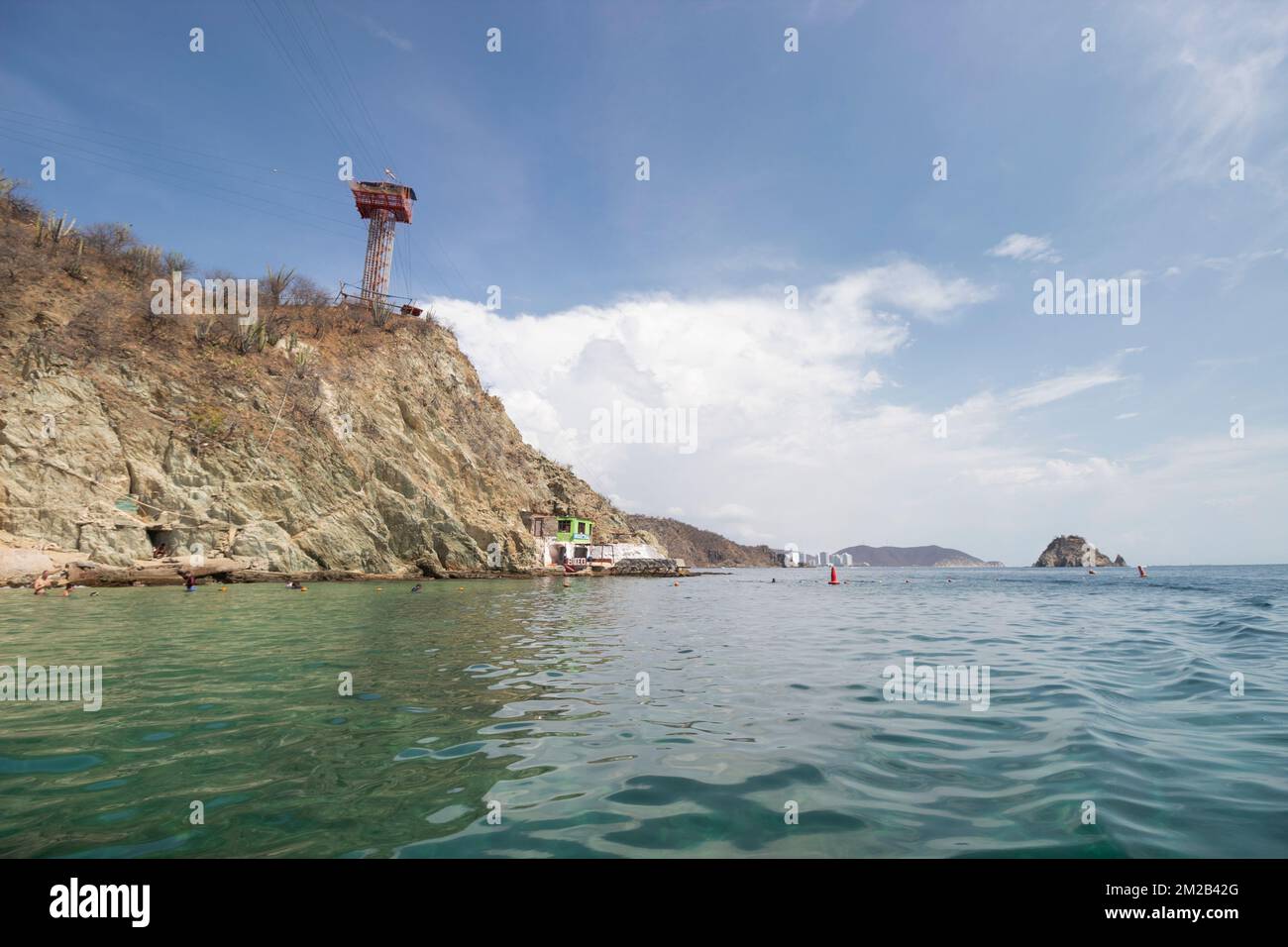 Playa Blanca oder weißer Strand an der englischen Küste mit blauem Meer, felsigen Hügeln, überdachtem Turm und Santa Marta colombia Stadt im Hintergrund. Stockfoto