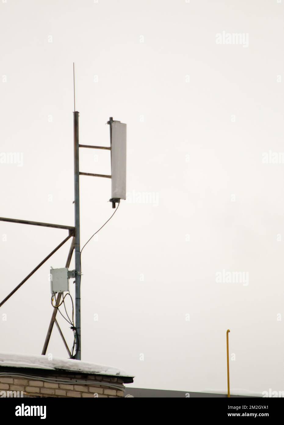 Eine Mobilfunkantenne auf dem Dach des Hauses sorgt für eine zuverlässige Verbindung. Schnee liegt auf dem Meilenstein, vor dem Hintergrund eines grauen Himmels. Bewölkt, kalter Wintertag, weiches Licht. Stockfoto