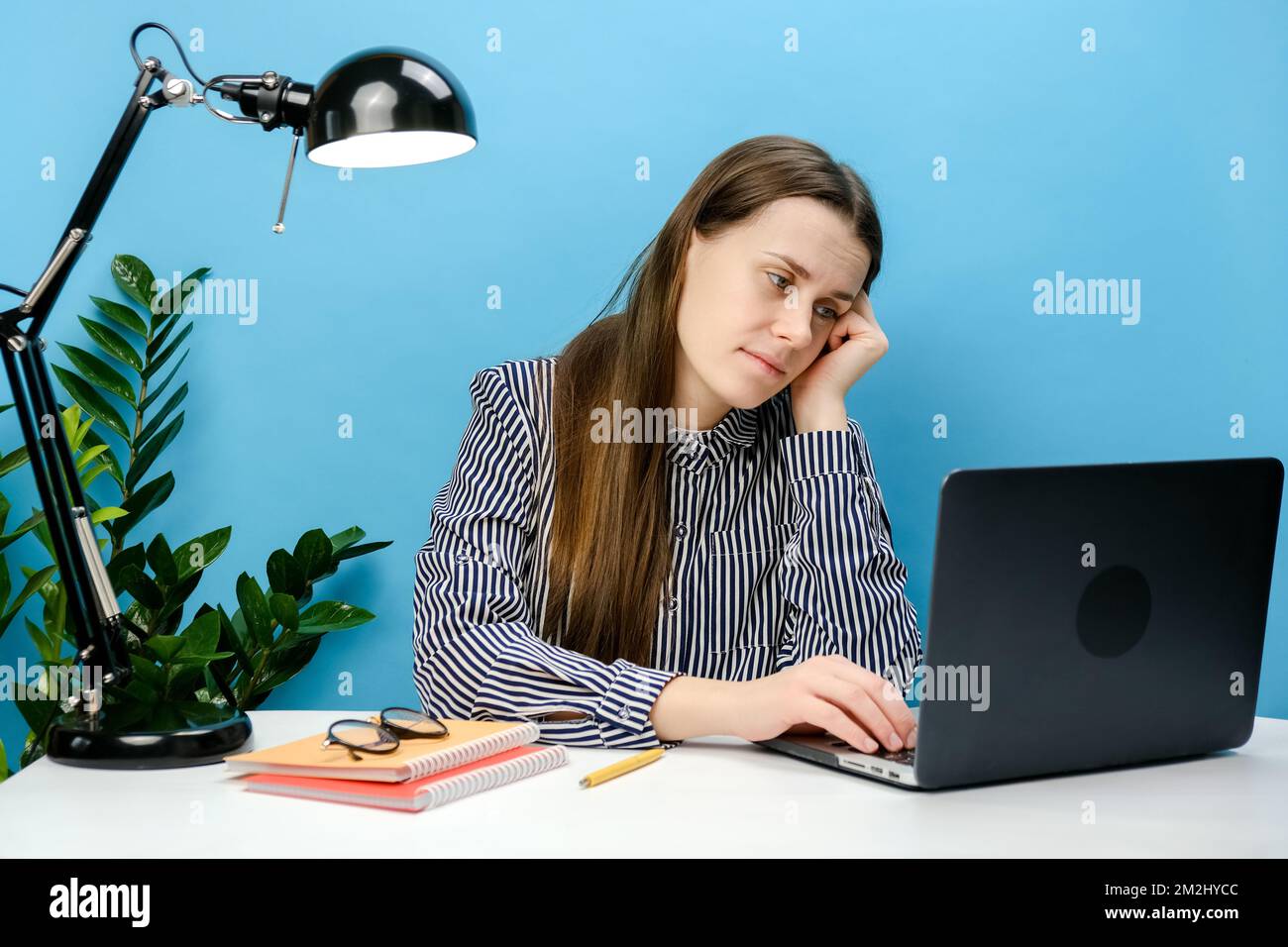 Verwirrt müde, frustrierte Sekretärin junge weibliche 20s in Hemd sitzende Arbeit an weißem Büroschreibtisch benutzen Laptop Internet-Requisiten-Gesicht und postieren isola Stockfoto