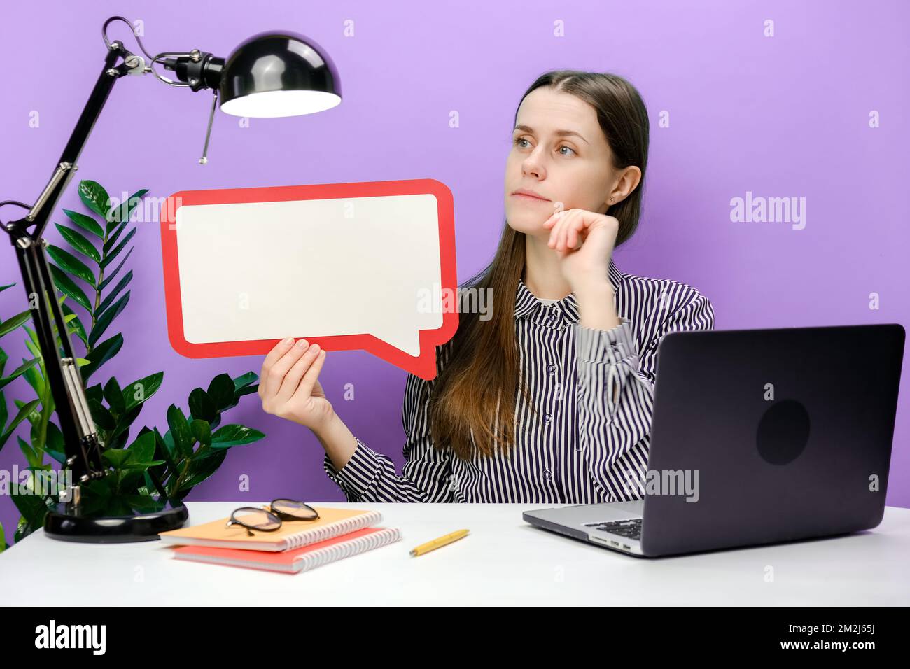 Eine junge Geschäftsfrau, die mit einem leeren Laptop am weißen Büroschreibtisch sitzt, sagt, dass die Sprechblase in der Cloud Werbematerial aufbaut Stockfoto