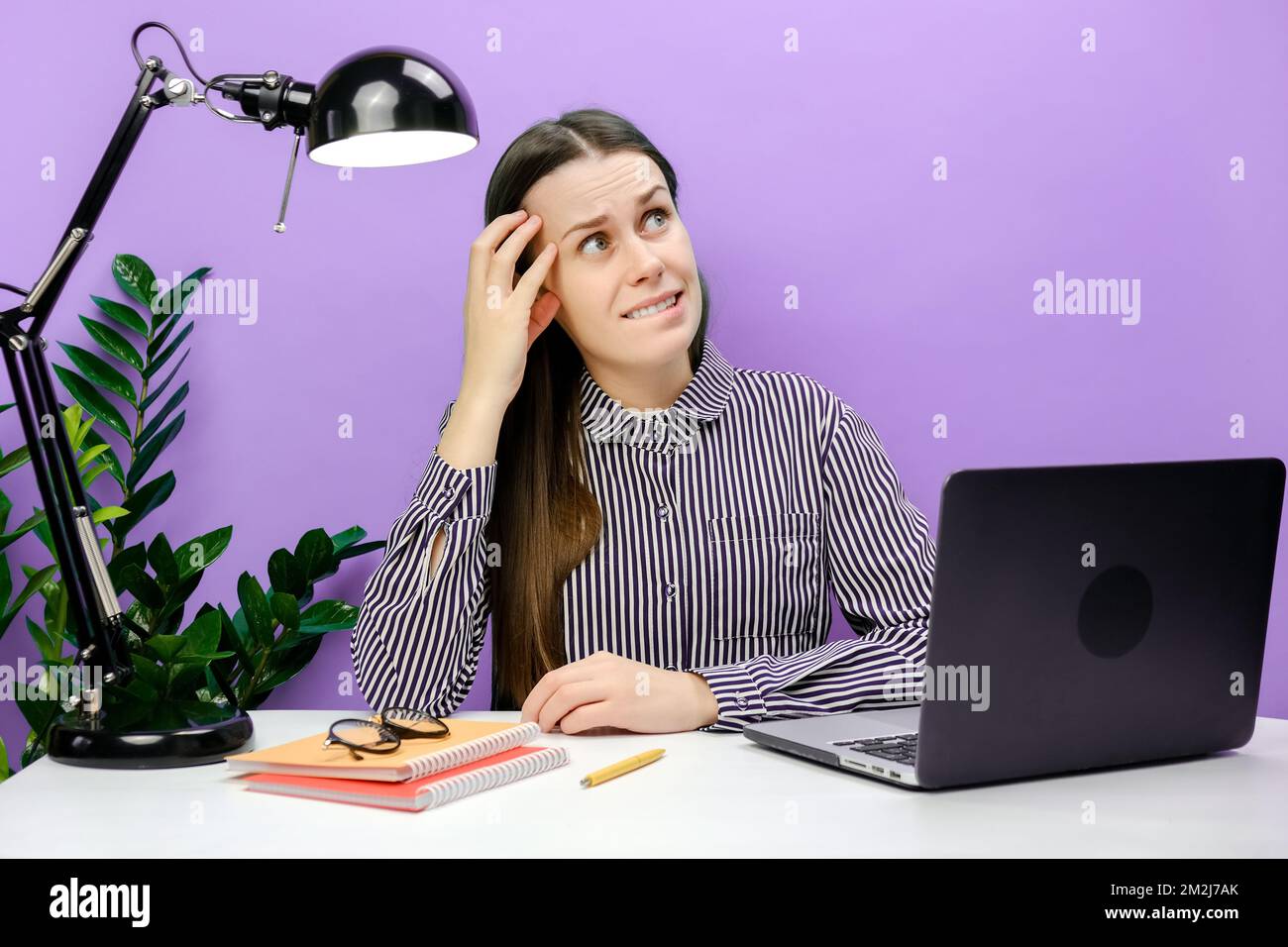 Porträt einer verstörten Sekretärin, eine junge Frau im Hemd, die am weißen Büroschreibtisch mit pc-Laptop sitzt, auf die Seite schaut und Isolat postet Stockfoto