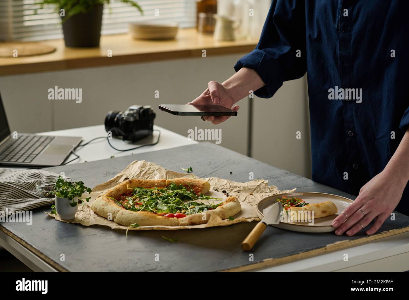 Nahaufnahme einer Fotografin, die während der Arbeit im Studio auf ihrem Smartphone ein Porträt von köstlicher Pizza macht Stockfoto