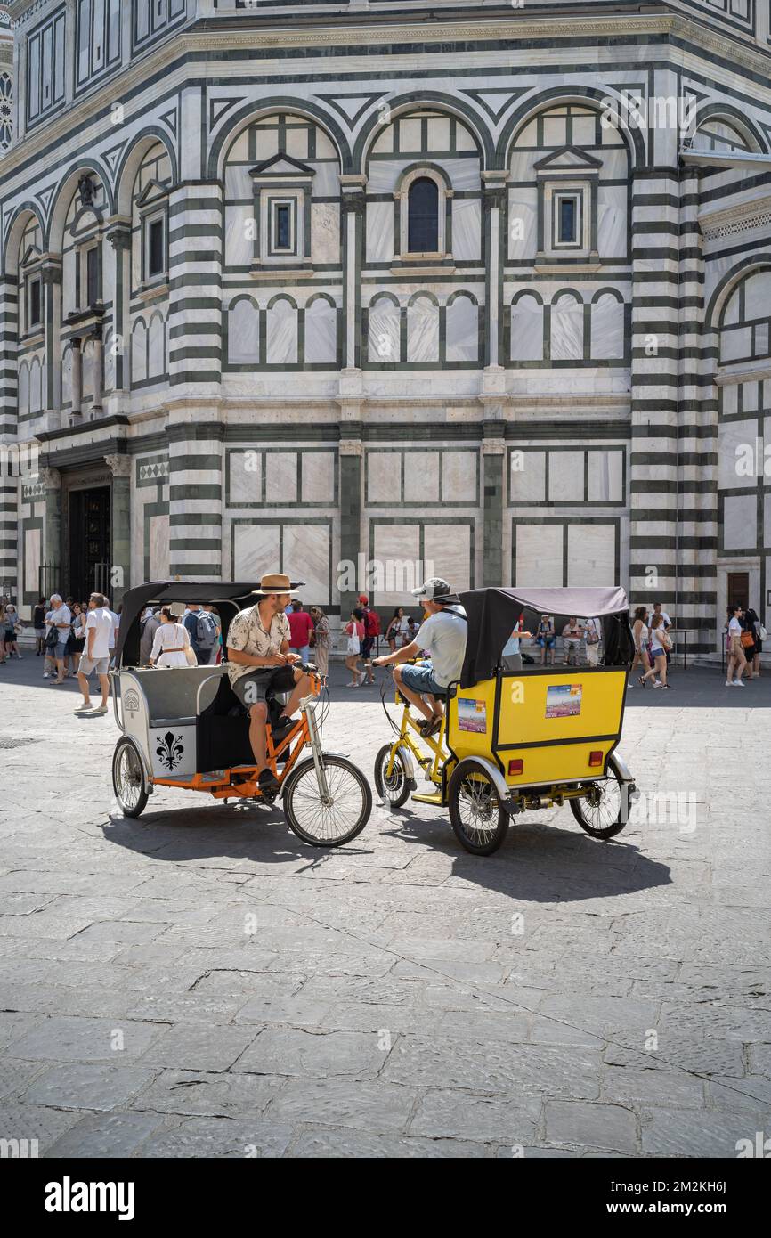 Florenz, Toskana/Italien - 15. Juni 2019: Zwei Rikscha-Fahrer, die auf ihrem Velo-Taxi vor dem Baptisterium von St. John in Florenz sitzen Stockfoto