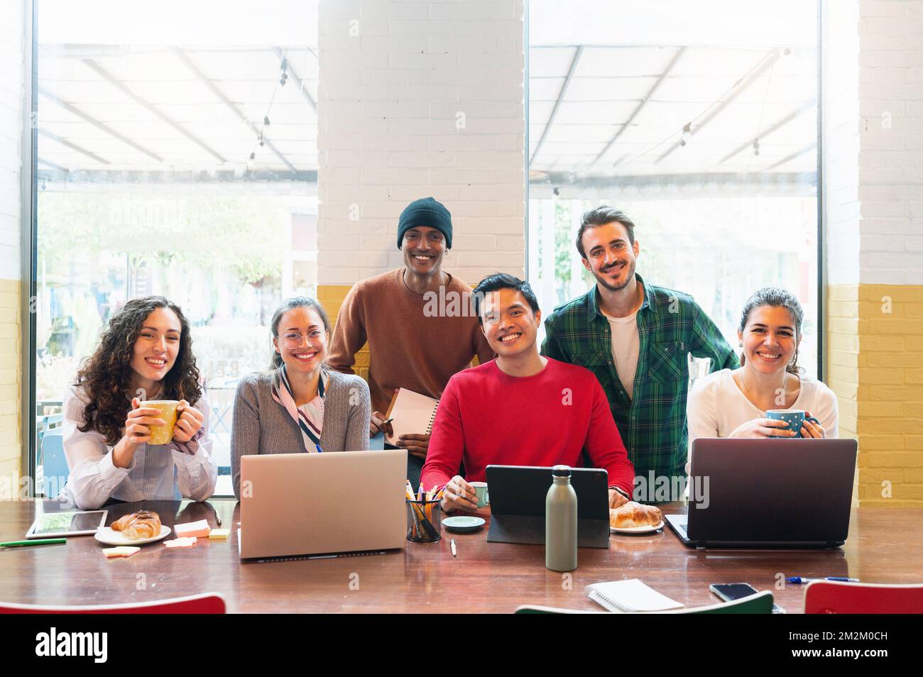 Multiethnische Gruppe junger Gelegenheitsmenschen, die Computer im Büro benutzen und vor der Kamera lächeln. Stockfoto