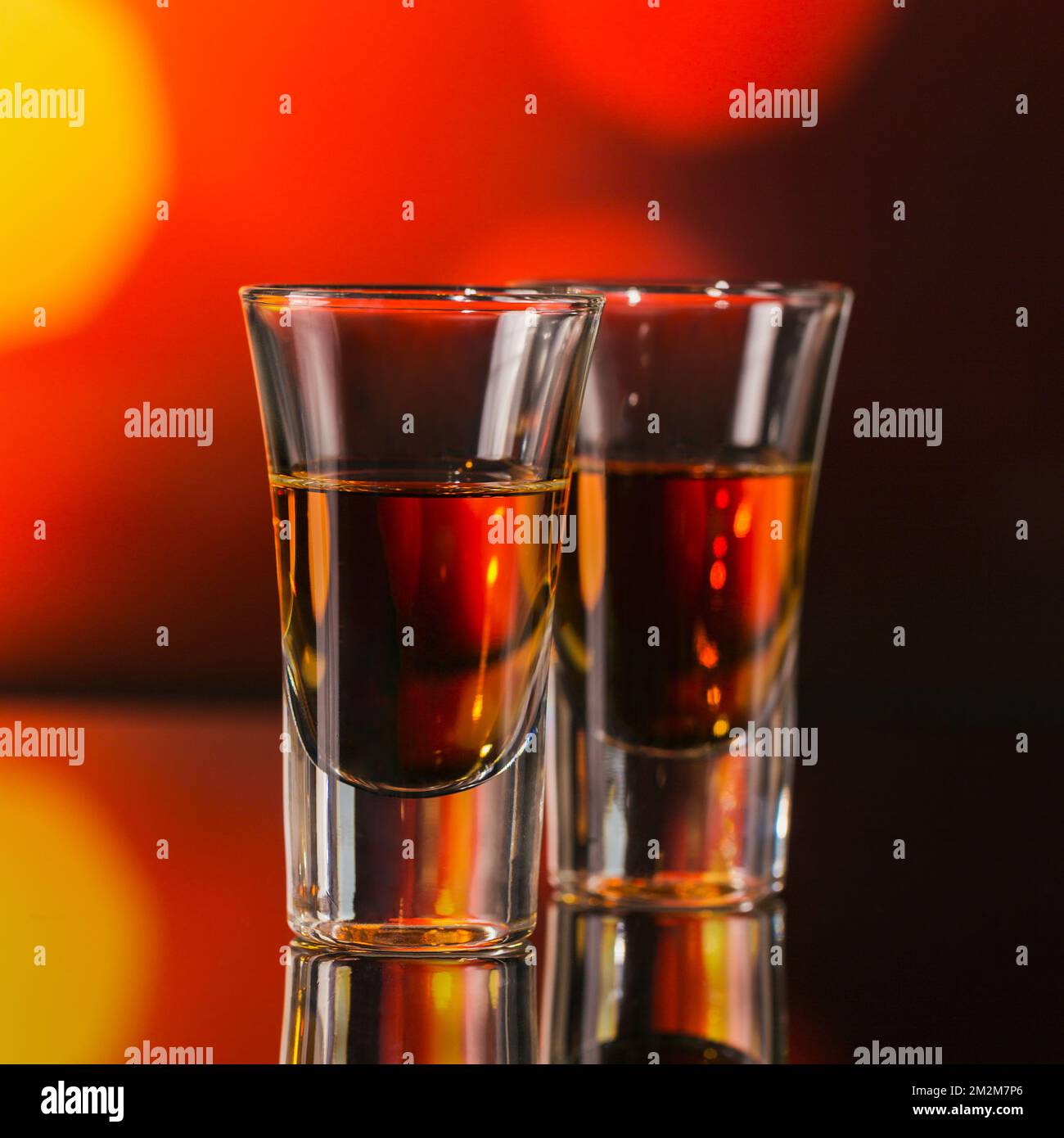Zwei Gläser Whiskey oder Bourbon auf rotem Bokeh-Hintergrund. Whiskey-Stimmungskonzept Stockfoto