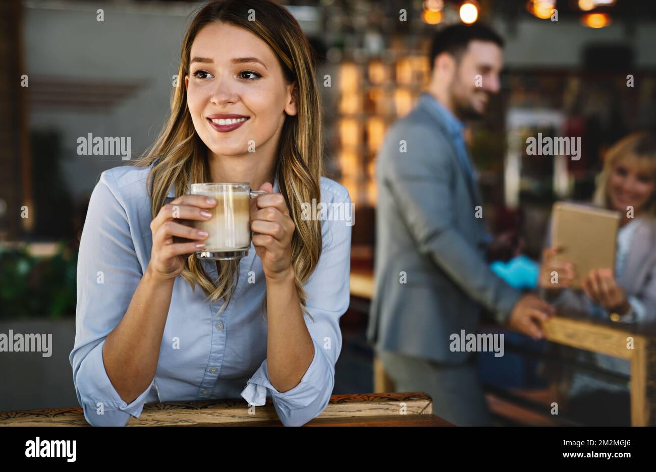 Porträt einer glücklichen jungen Geschäftsfrau, die in einer Pause Kaffee trinkt. Im Hintergrund ihre Kollegen Stockfoto