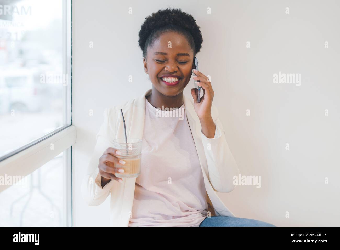 Healthy young businesswoman with glass of fresh beverage, speaking on mobile phone while consulting client sitting in cafe. Cute lady having phone Stockfoto