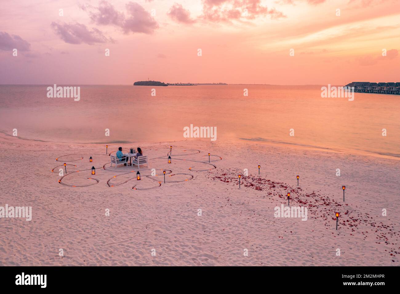 Fantastisches romantisches Abendessen am Strand mit Kerzen und Blumen unter dem Himmel des Sonnenuntergangs. Romantik und Liebe, luxuriöses Restaurant, exotische Tischgestaltung Stockfoto