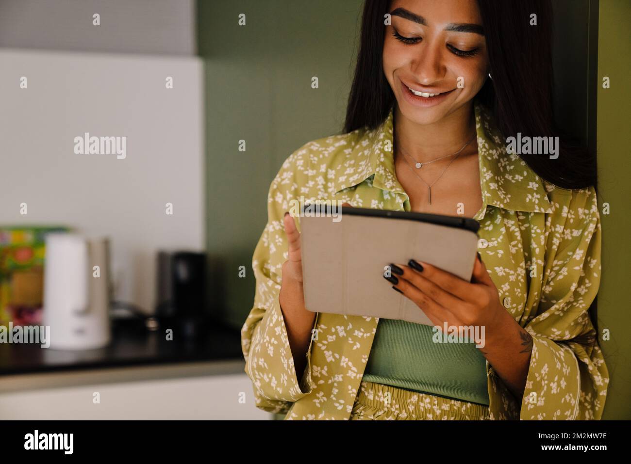 Junge, attraktive, langhaarige, lächelnde Frau, die zu Hause mit einem Tablet steht Stockfoto