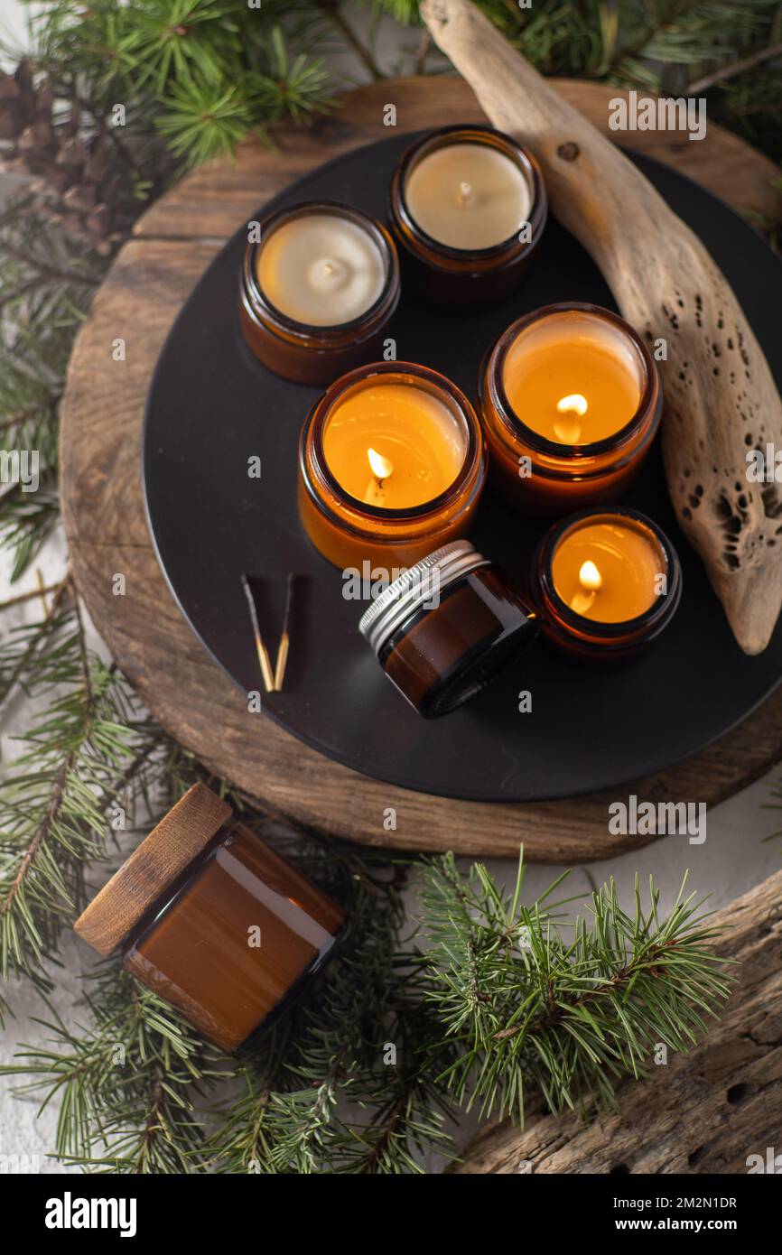 Sojalkerzen brennen in Gläsern. Komfort zu Hause. Kerze in einem braunen Glas. Duft und Licht. Handgemachte Duftkerze. Aromatherapie. Weihnachtsbaum und Winterstimmung. Gemütliche Einrichtung. Festliche Dekoration Stockfoto