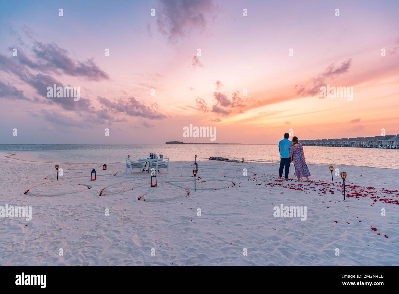 Fantastisches romantisches Abendessen am Strand mit Kerzen und Blumen unter dem Himmel des Sonnenuntergangs. Romantik und Liebe, luxuriöses Restaurant, exotische Tischgestaltung Stockfoto