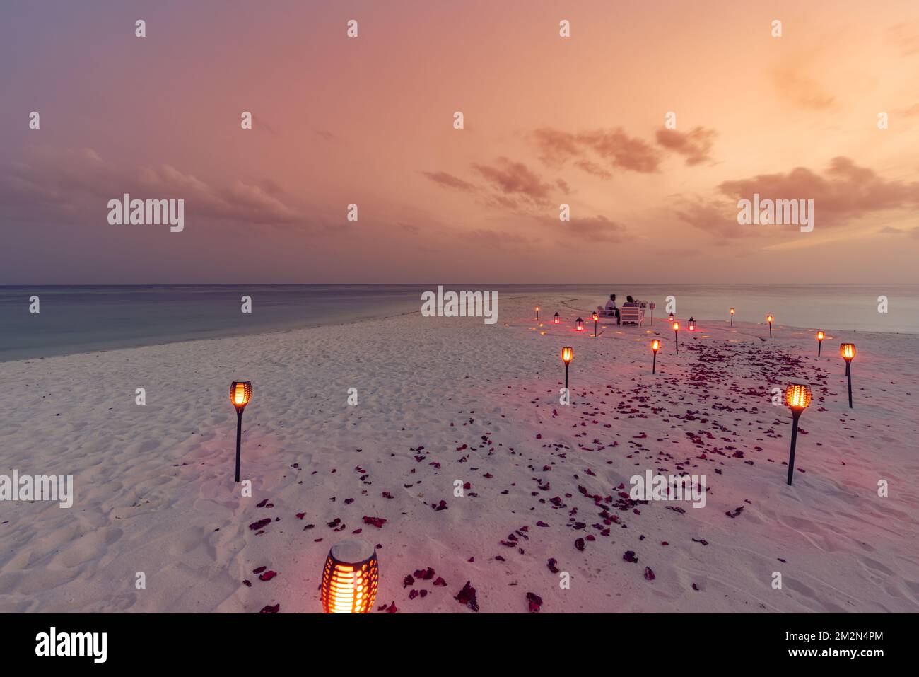 Fantastisches romantisches Abendessen am Strand mit Kerzen und Blumen unter dem Himmel des Sonnenuntergangs. Romantik und Liebe, luxuriöses Restaurant, exotische Tischgestaltung Stockfoto