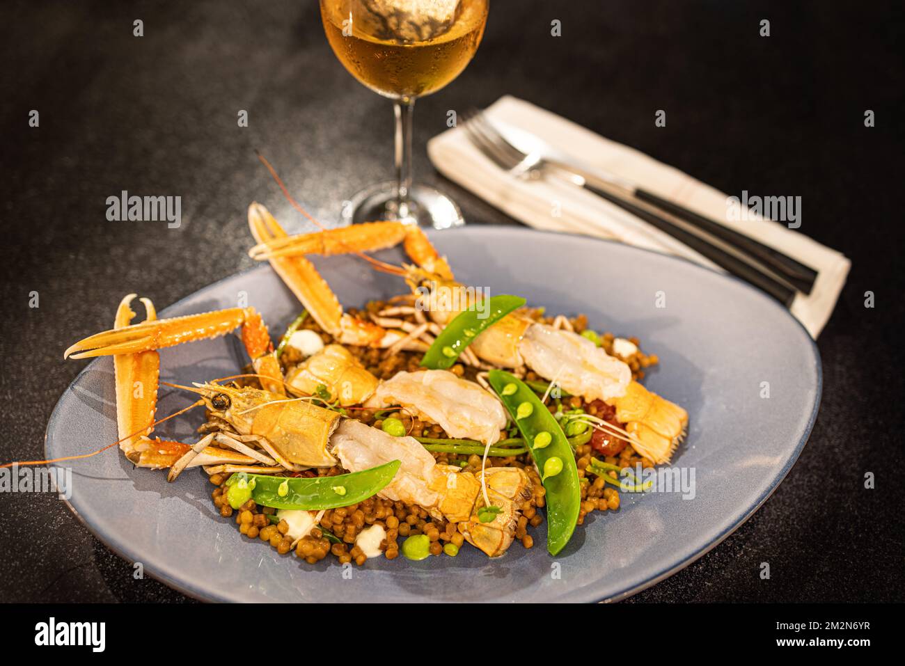 Gekochte Garnelen mit Erbsen und Sauce auf einem eleganten Teller mit Rosenwein. Luxuriöse Gourmet-Dinner-Vorspeise Stockfoto