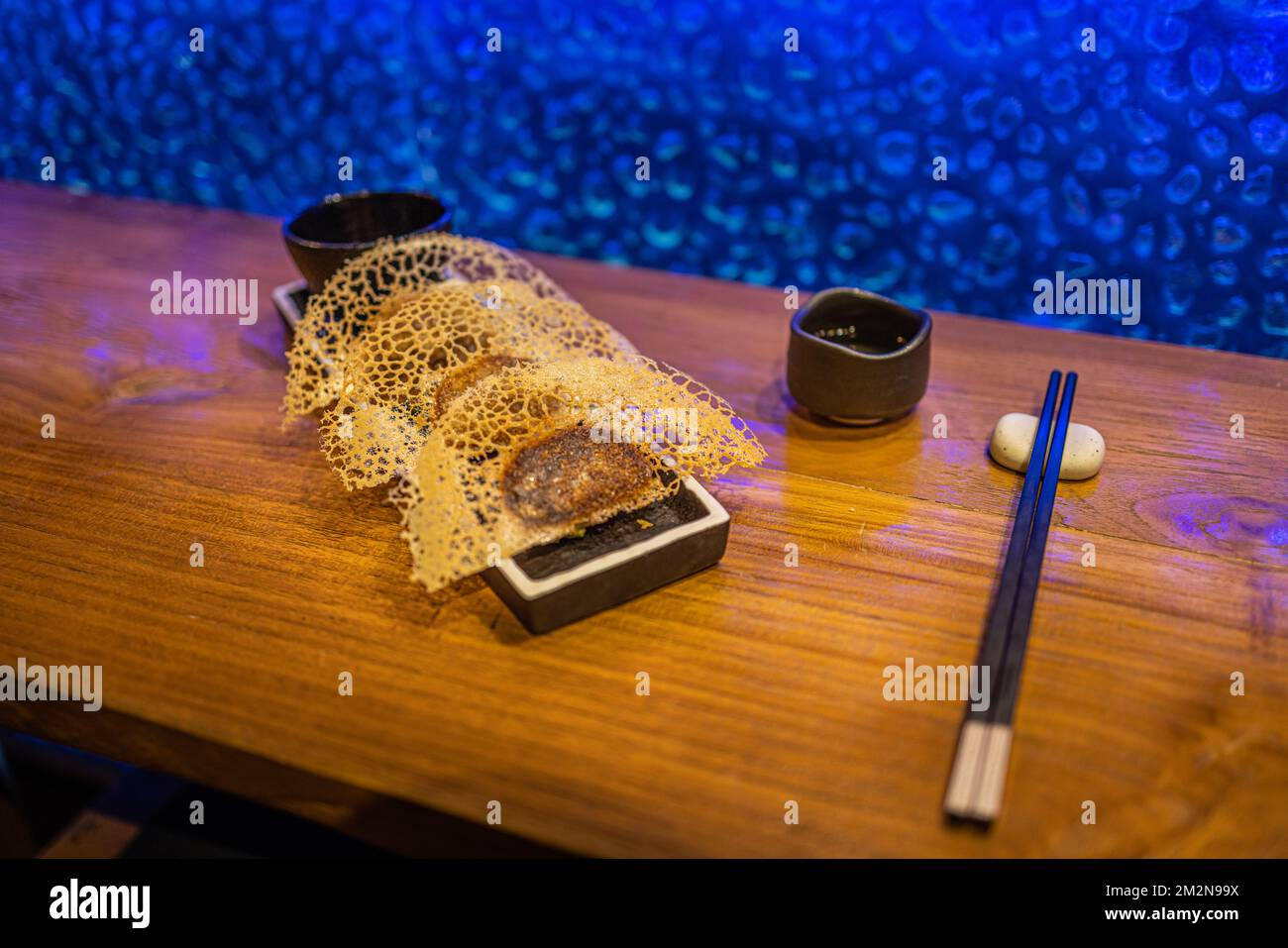 In der Pfanne gebratene Gyoza-Teigtaschen auf rustikalem Holzhintergrund im Luxusrestaurant. Exklusive Gourmetgerichte im Hintergrund. Japanische Küche im künstlerischen Design Stockfoto