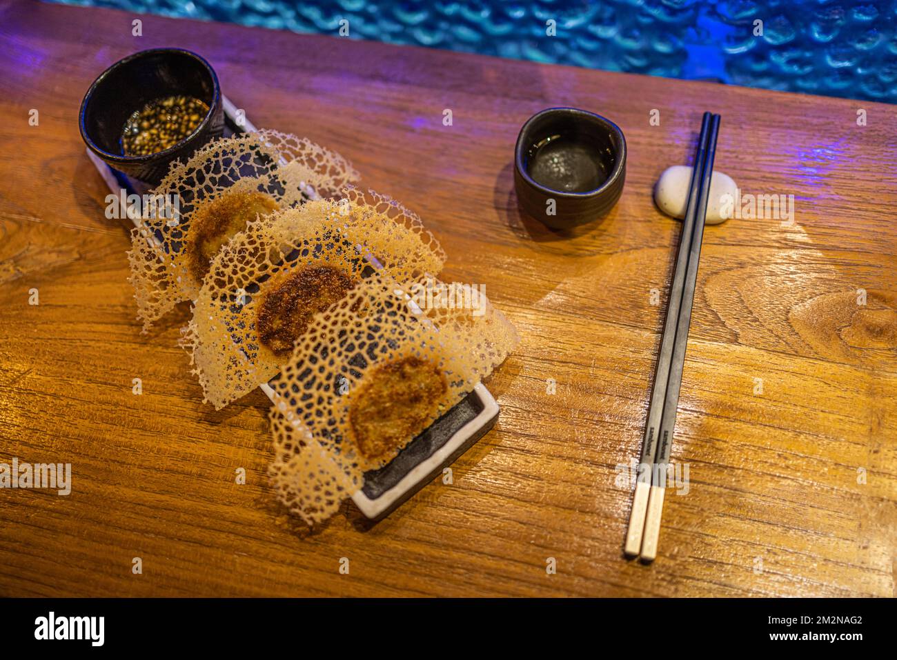 In der Pfanne gebratene Gyoza-Teigtaschen auf rustikalem Holzhintergrund im Luxusrestaurant. Exklusive Gourmetgerichte im Hintergrund. Japanische Küche im künstlerischen Design Stockfoto