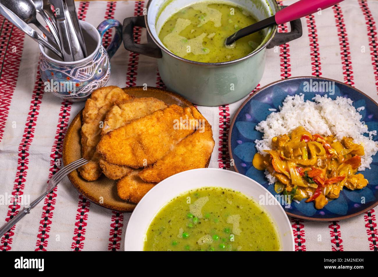 Mittag- oder Abendessen mit vielen Mahlzeiten. Erbsensuppe, paniertes gebratenes Fleisch (Schnitzel) und asiatisches Hühnchen-Curry mit Reis. Stockfoto