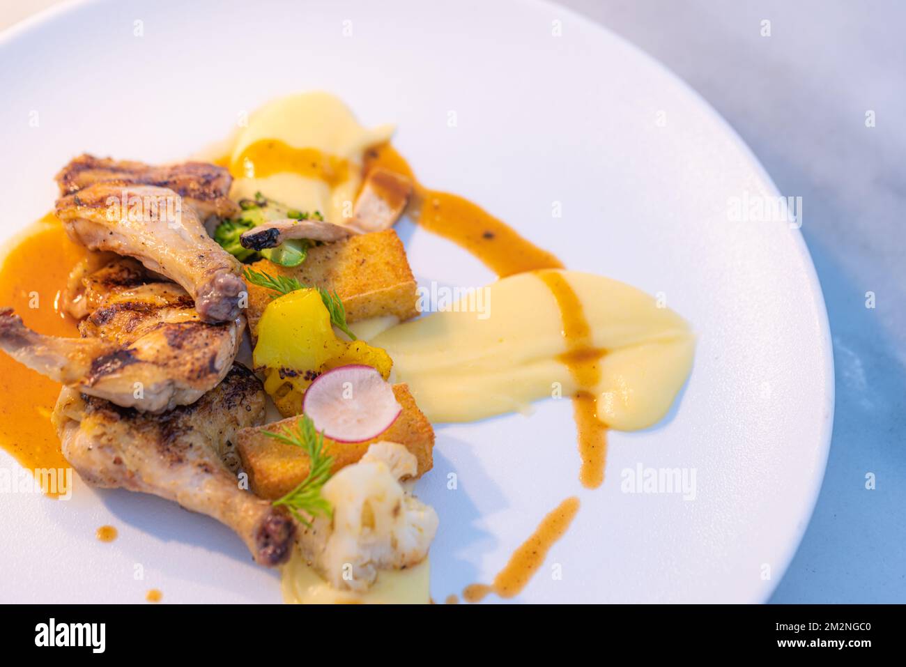 Gegrillte Hähnchenschenkel mit Gewürzen und frischem Gemüse und zerbrochenen Kartoffeln. Gourmetküche im Hintergrund mit eleganter Tischplatte und sanfter Beleuchtung Stockfoto