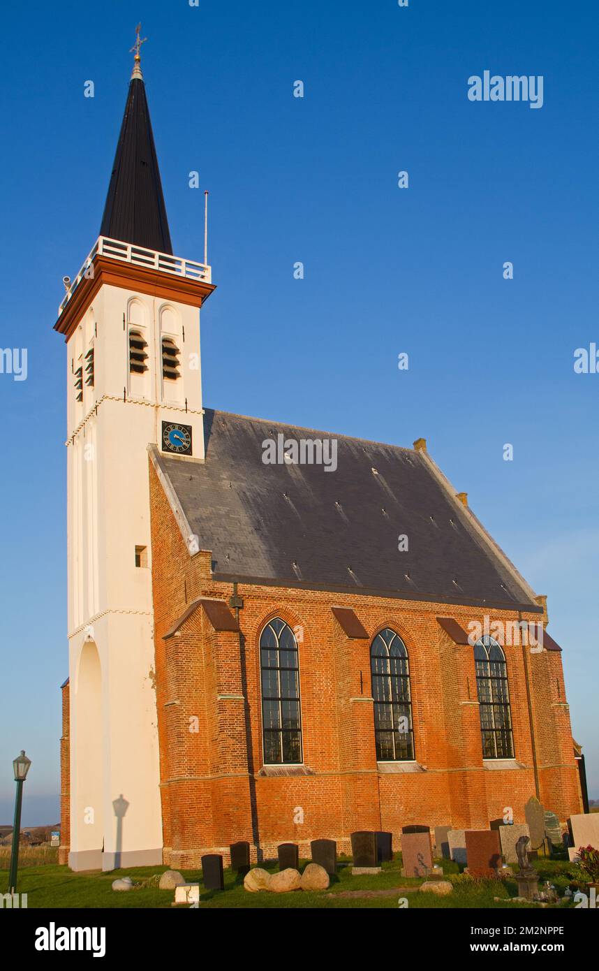 Mittelalterliche Backsteinkirche mit weißem Turm, umgeben von einem Friedhof, unter blauem Himmel Stockfoto